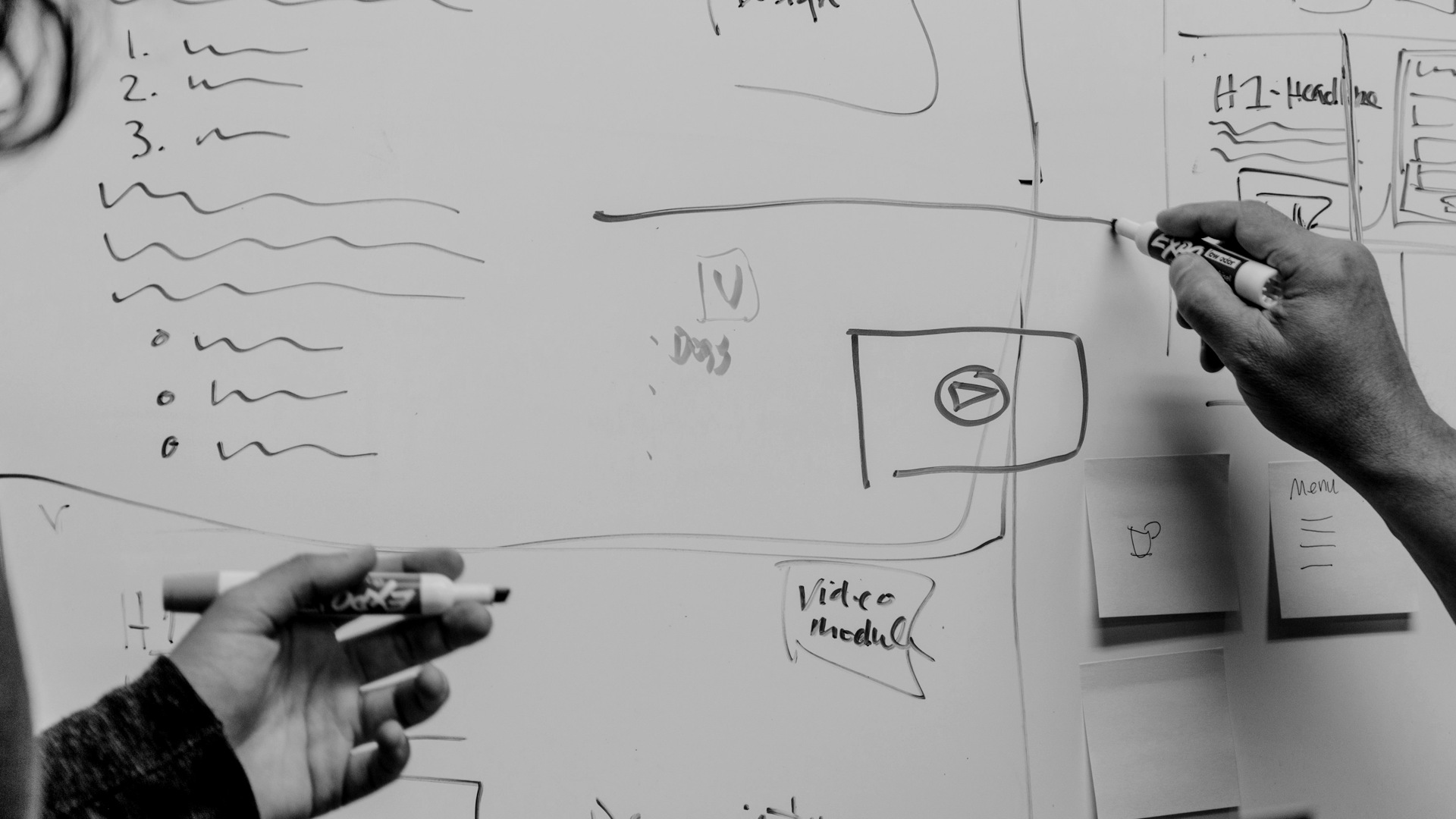 Home 6 Two people drawing and discussing ideas on a whiteboard, shown in monochrome.