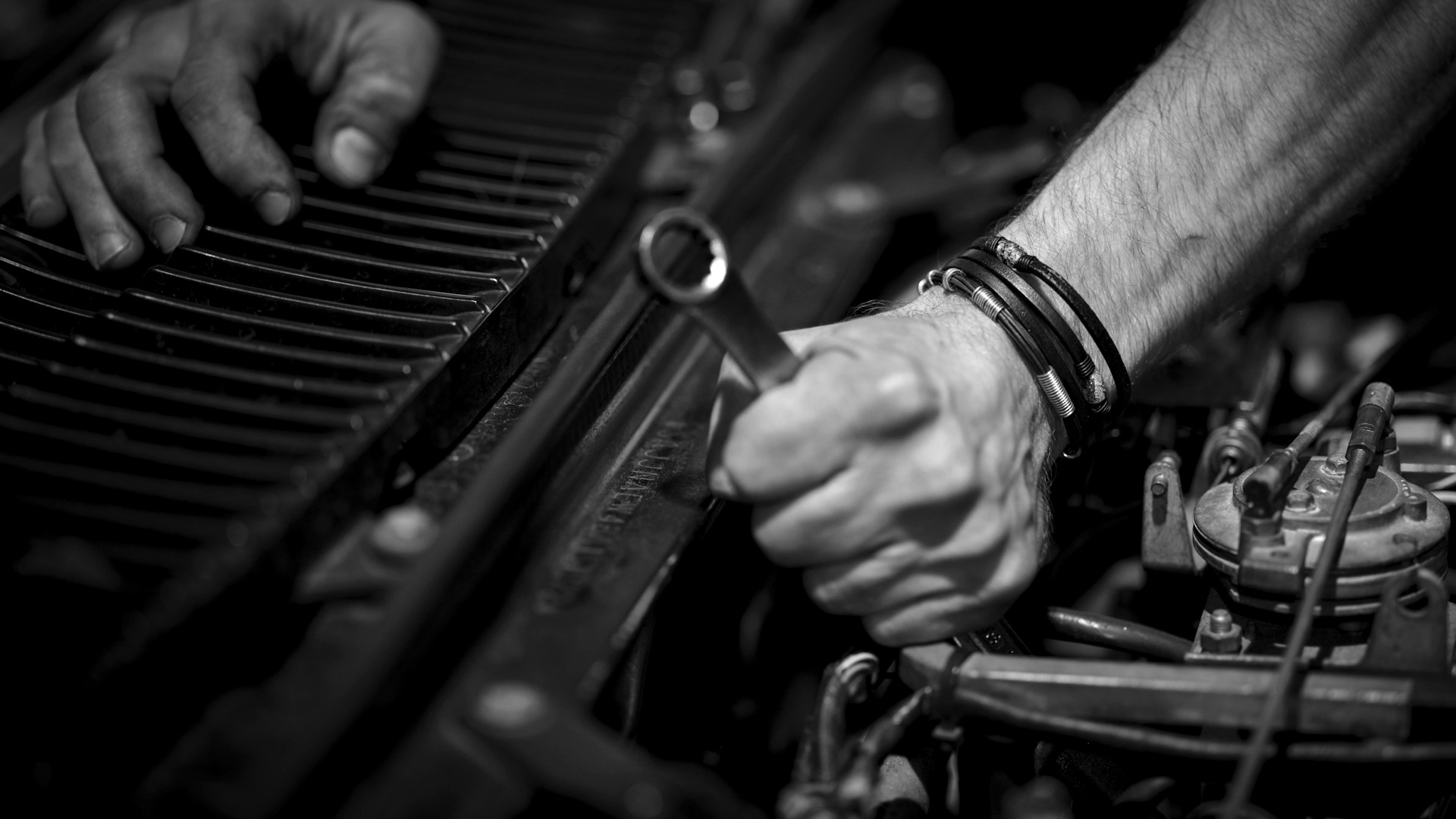 Hands with grease working on a car engine with a metal wrench.