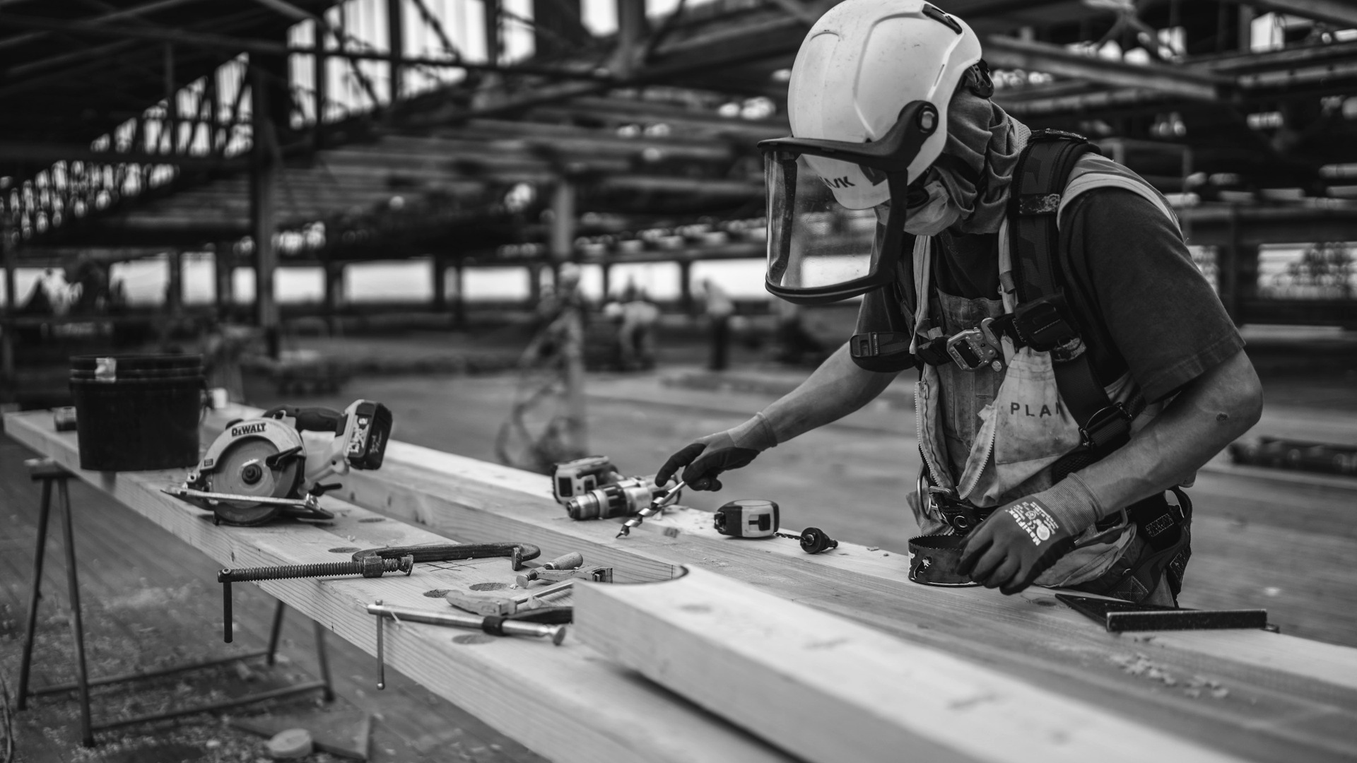 Man in orange and black vest wearing white helmet holding yellow and black power tool.