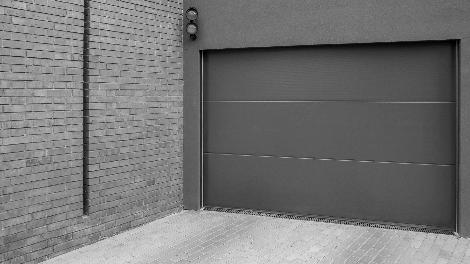 A grey garage door next to a brick wall.