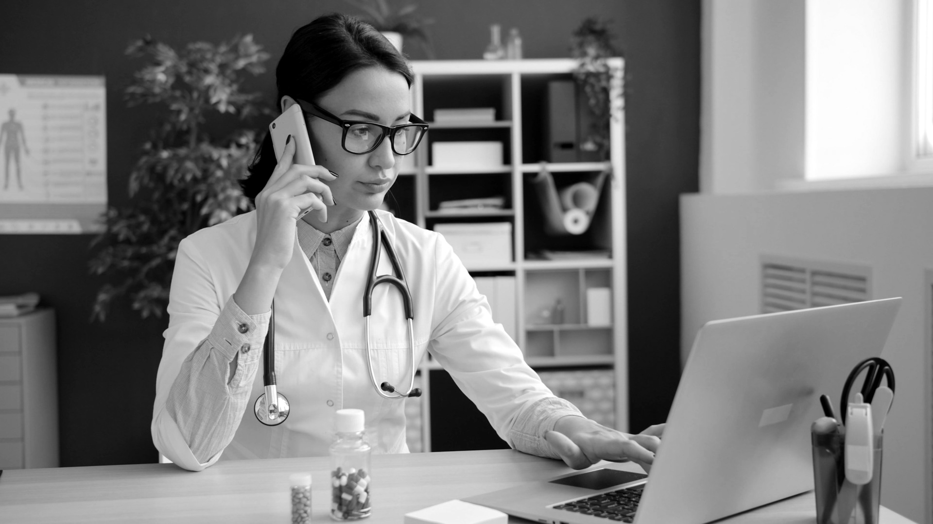 Doctor on phone, working on laptop in office.
