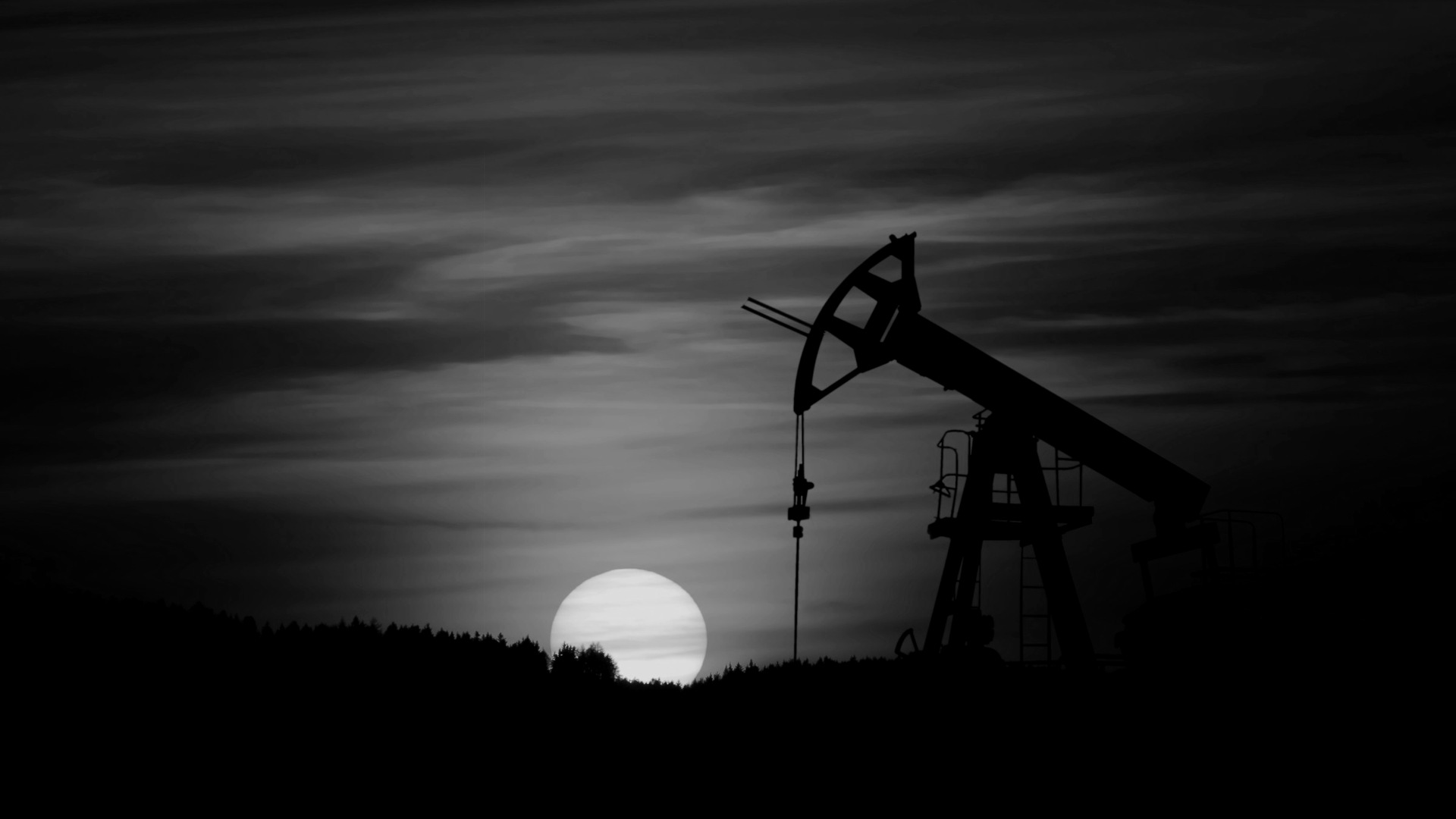 Oil pump jack silhouette against red sunset.