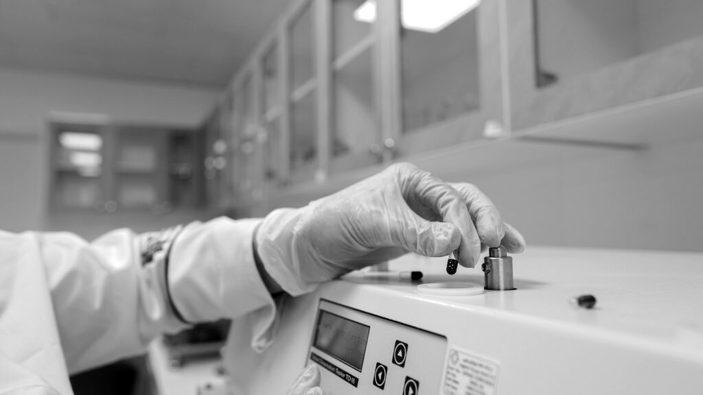 A person in a lab coat and gloves working on a machine.