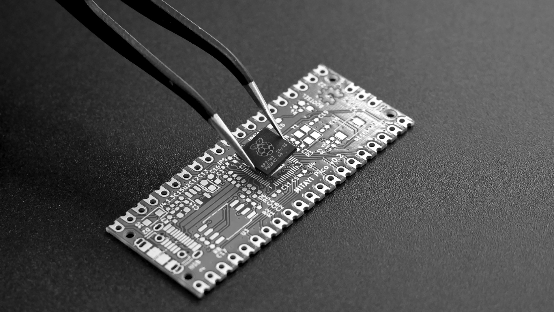 Tweezers placing a small black microchip onto a green circuit board.