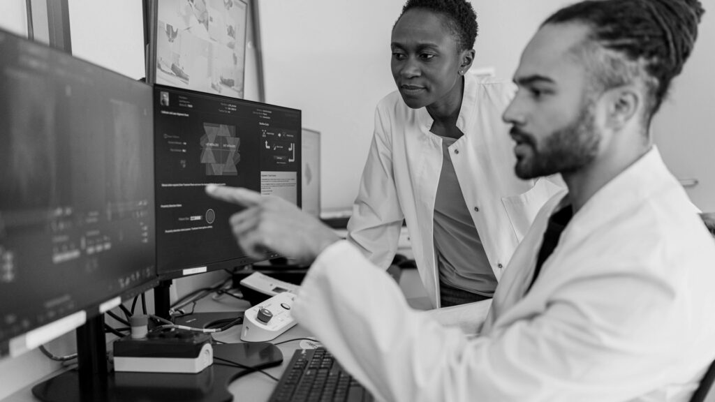 Two medical professionals in white coats reviewing digital imaging on computer monitors.
