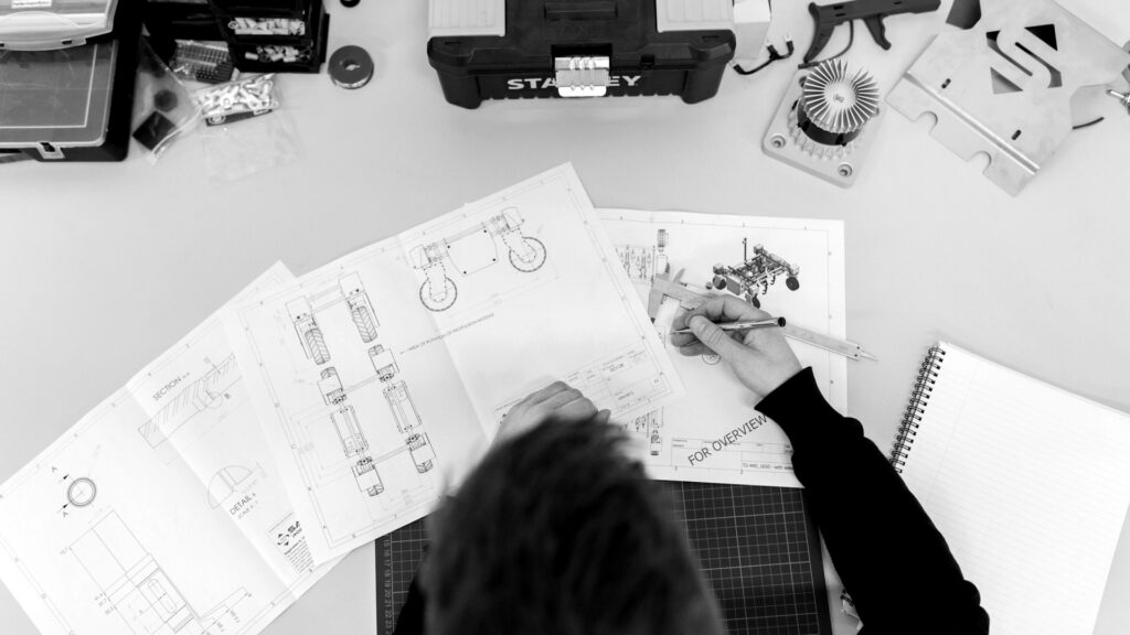 A person using a caliper to measure technical engineering drawings on a desk.