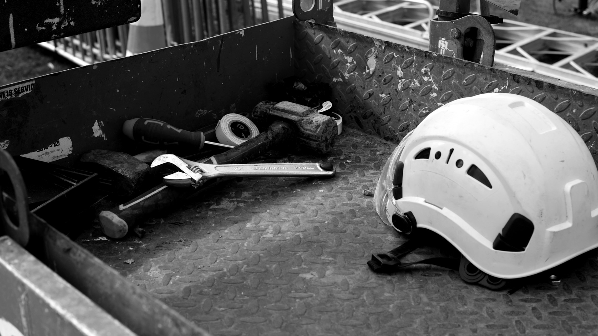 A white hard hat and various construction tools inside a red metal container.