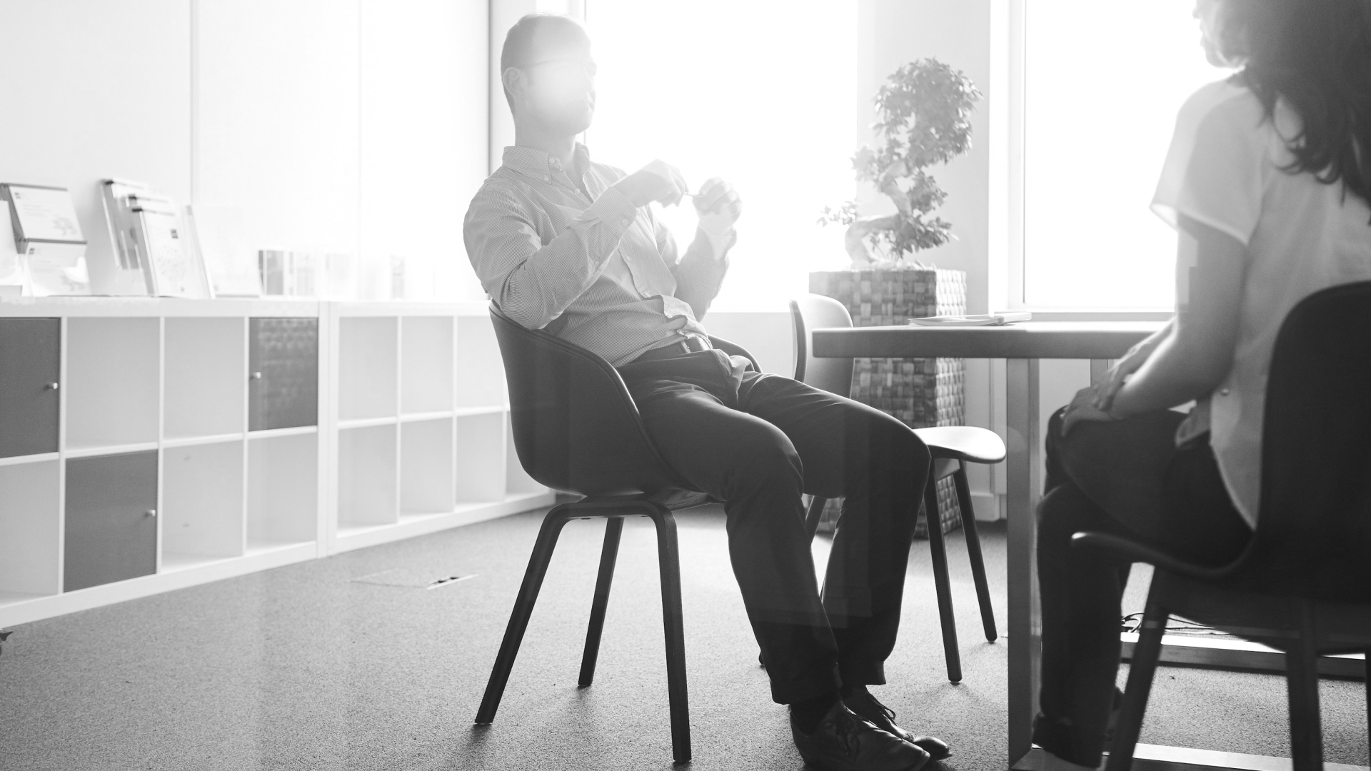 Home 5 Two people seated in conversation in a bright office, shown in monochrome.
