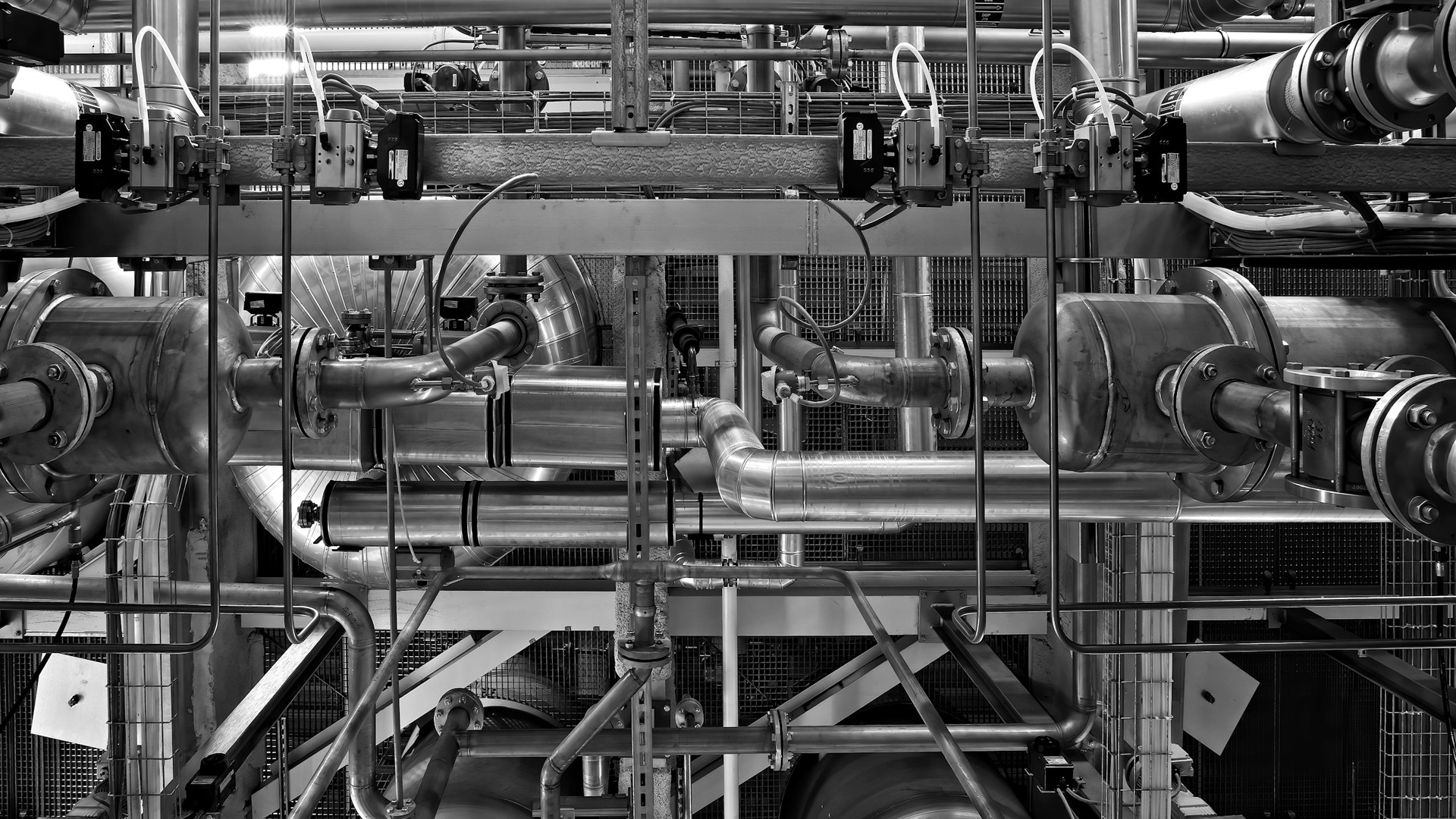 A complex network of industrial metal pipes and valves in a factory setting.