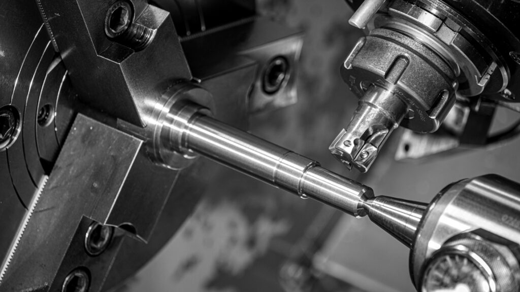 A metal rod held in a lathe chuck being machined by a cutting tool.