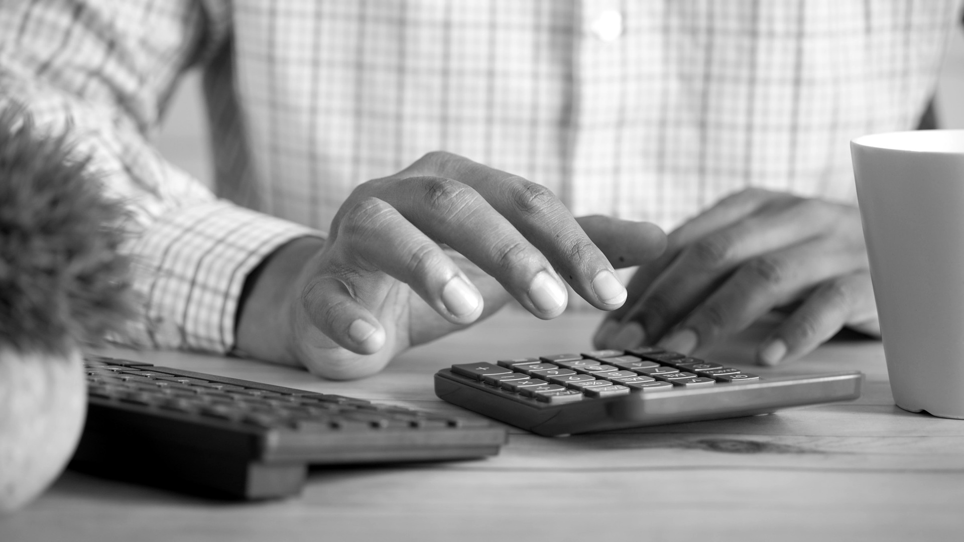 Person using calculator at desk with coffee mug.